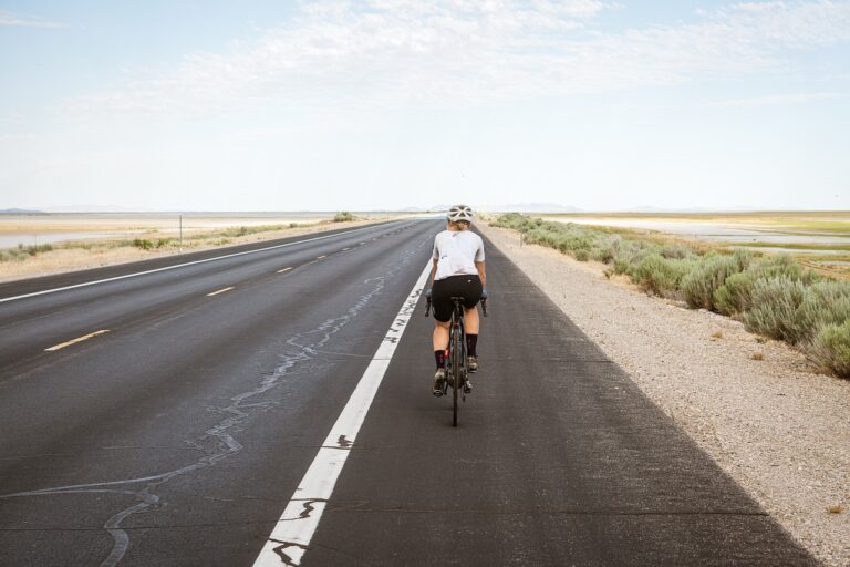 Cycliste solitaire roulant sur une route ouverte, entourée de paysages désertiques et vastes plaines, symbolisant la liberté et l'évasion offertes par le vélo. LovingBike.com